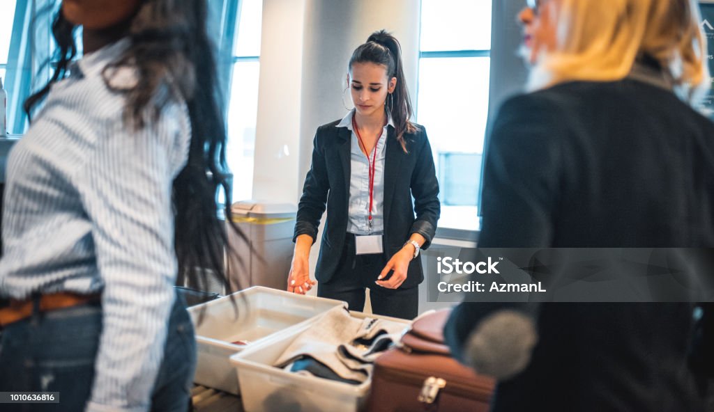 Female security staff checking luggage of passengers. Midsection of travelers are standing during security check. They are at airport terminal.
