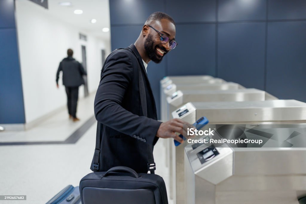 Smiling businessman using his smartphone while passing through an electronic ticket gate at the airport, eagerly preparing for an exciting journey ahead